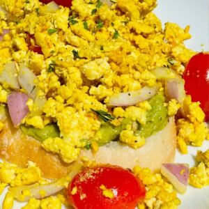 Easy tofu scramble on spicy avocado toast topped with cherry tomatoes, red onions, and herbs – high-protein vegan breakfast idea.