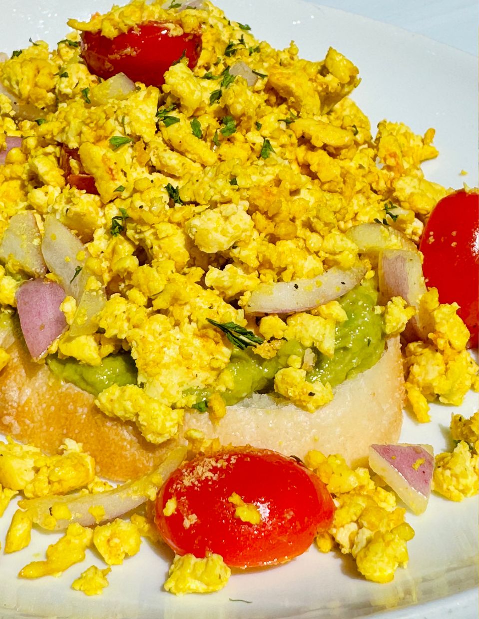 Easy tofu scramble on spicy avocado toast topped with cherry tomatoes, red onions, and herbs – high-protein vegan breakfast idea.